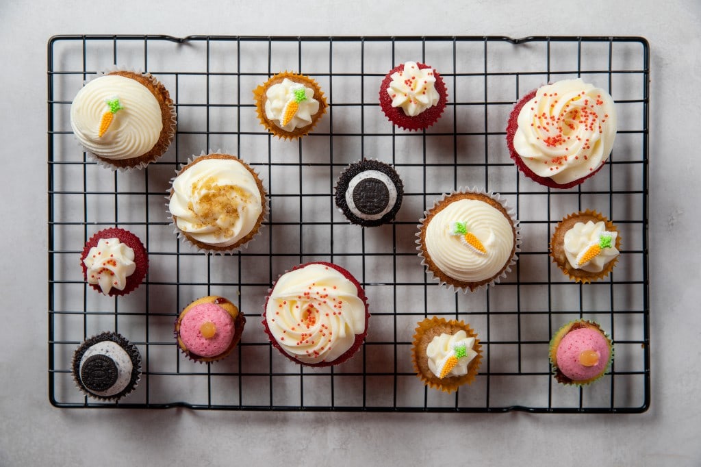 An assortment of full-size and mini Arble cupcakes arranged across a cooling rack