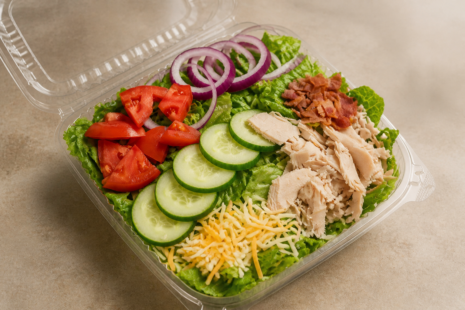 An Arble chef salad with lettuce, tomato, cucumber, red onion, turkey, bacon, and shredded cheese