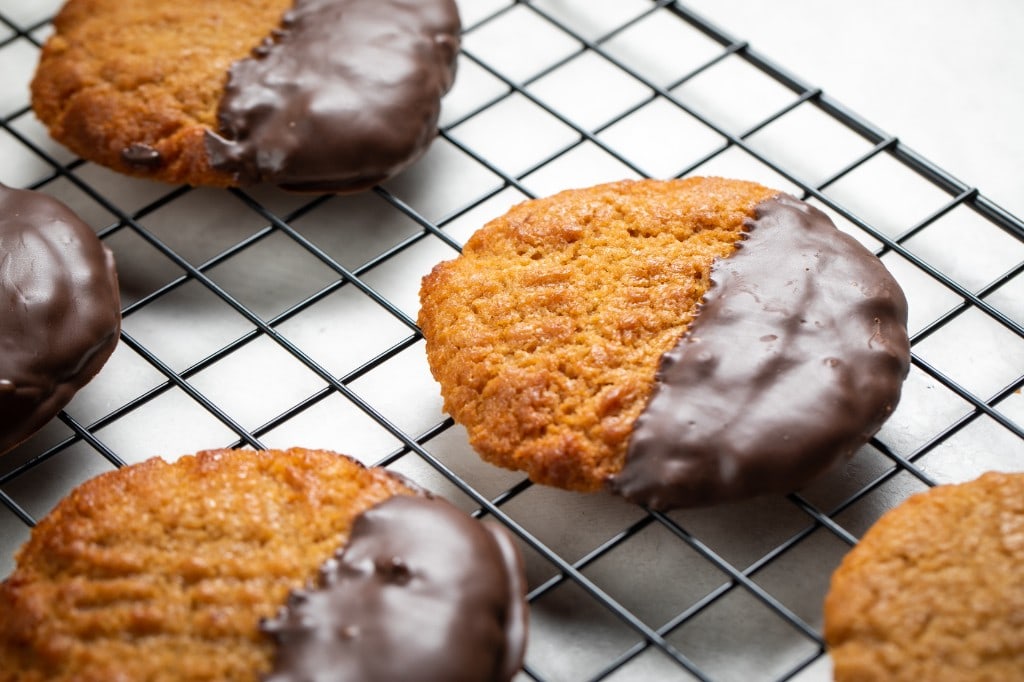 Fresh-baked peanut butter cookies dipped halfway in chocolate and cooling on a wire rack
